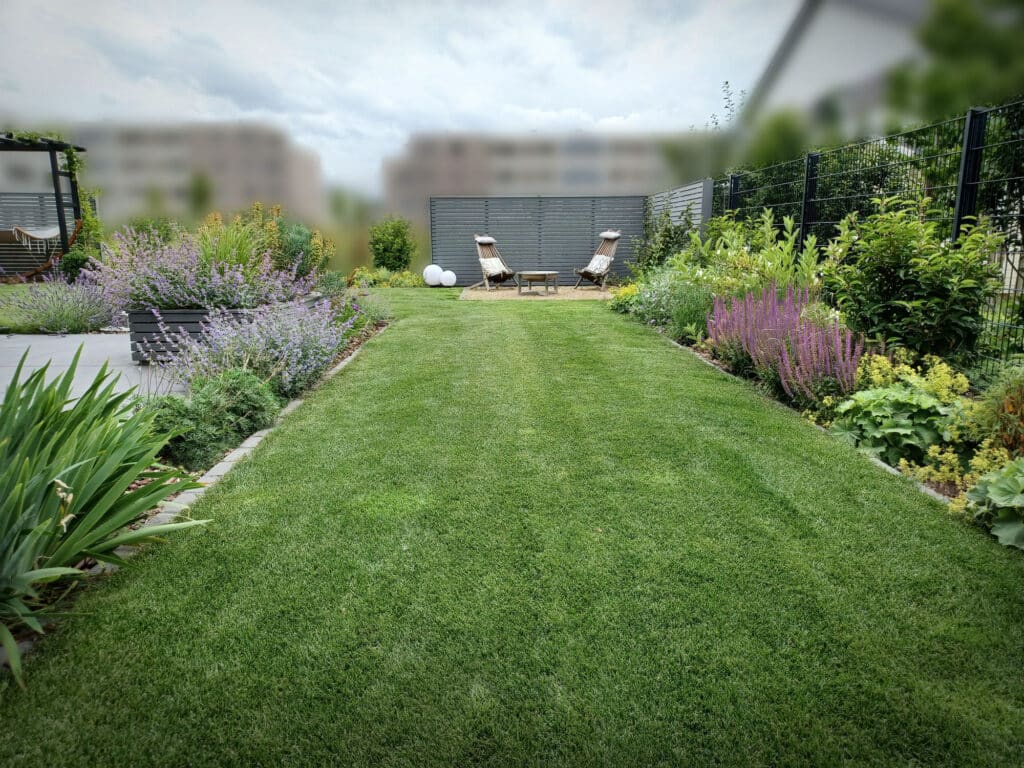 Nachher Bild von Gartendesign Minter: ordentliche und gepflegte Rasenfläche, bepflanzte Beete und Sitzecke im Hintergrund