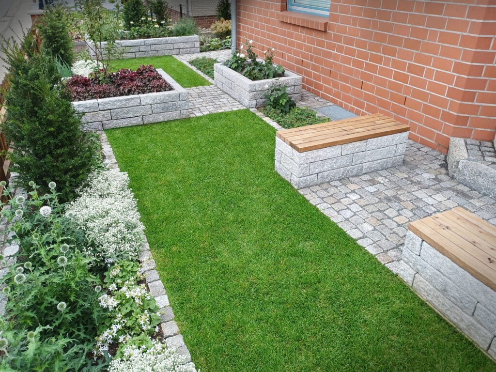 gut gepflegte Rasenfläche, gesäumt von schön bepflanzten Beeten und modernen Steinbänken