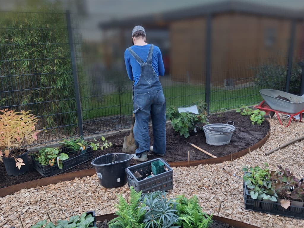 Ausführung der Gartengestaltung: Person mit Rücken zur Kamera steht mit Schaufel in einem Beet